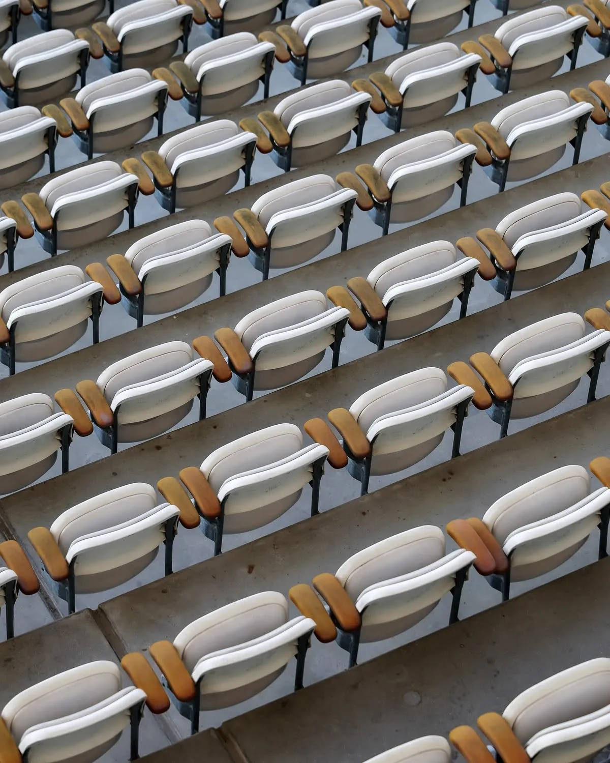Rzędy jasnych krzesełek na trybunie stadionu z lotu ptaka.