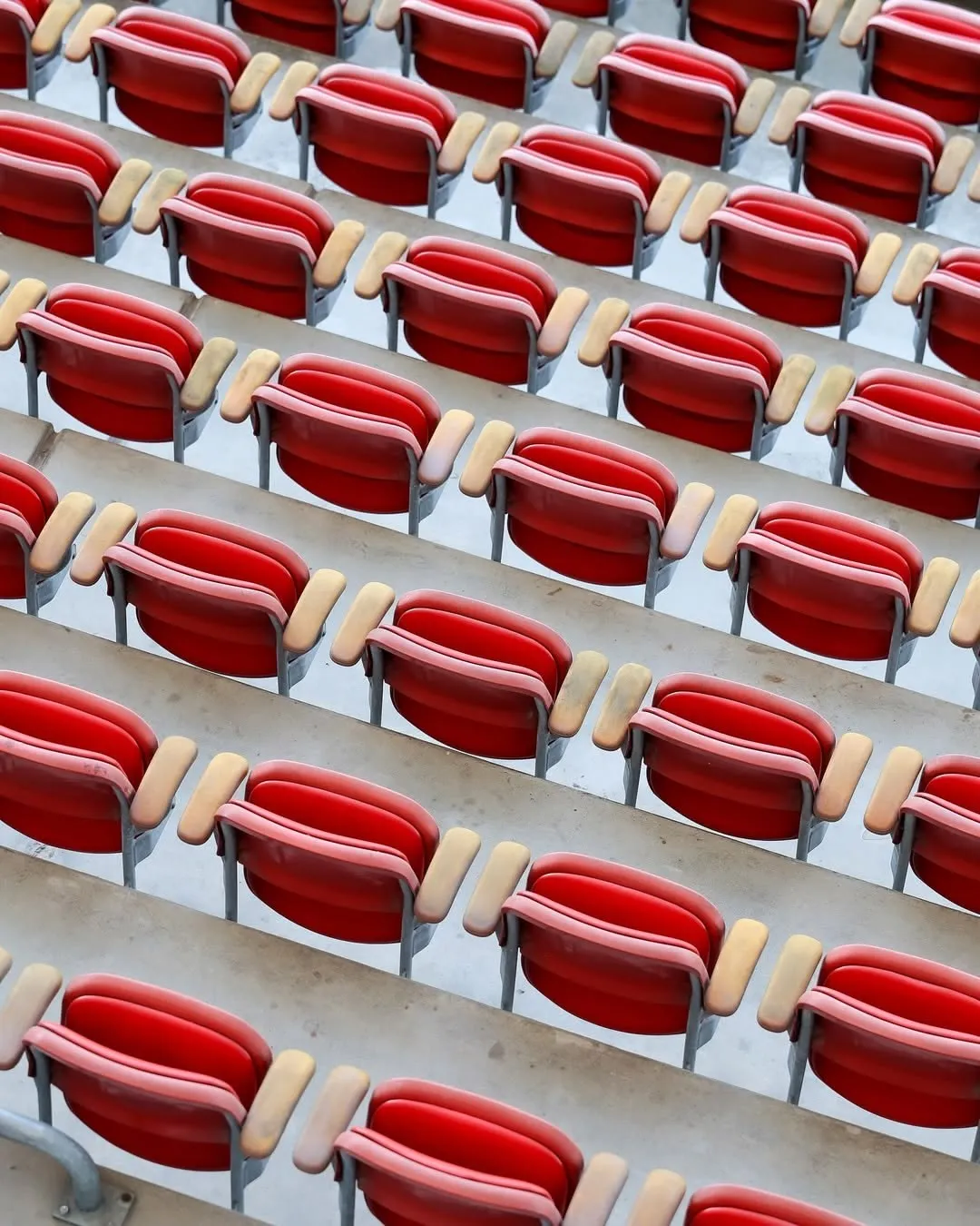 Rzędy czerwonych krzesełek na trybunie stadionu.