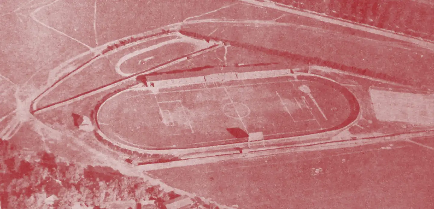 Archiwalne, czerwono tonowane zdjęcie lotnicze stadionu z bieżnią lekkoatletyczną okalającą murawę.